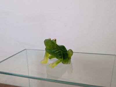 une figurine de grenouille verte posée sur une table en verre