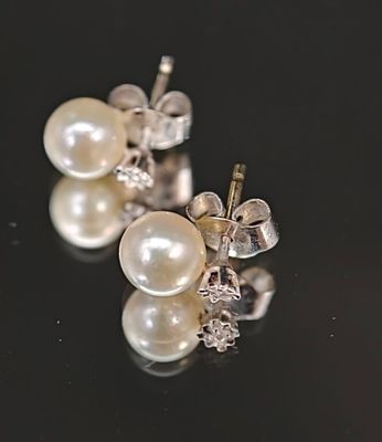 une paire de boucles d'oreilles en perles et diamants posées sur un fond noir
