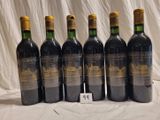 six bottles of red wine are lined up on a table
