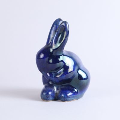 a small blue rabbit figurine sitting on a white surface