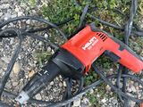 a corded drill laying on the ground next to a patch of grass