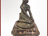 une statue en bronze représentant une femme assise sur un socle en marbre
