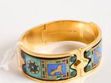 gold bracelet with blue and green designs on it on a white surface