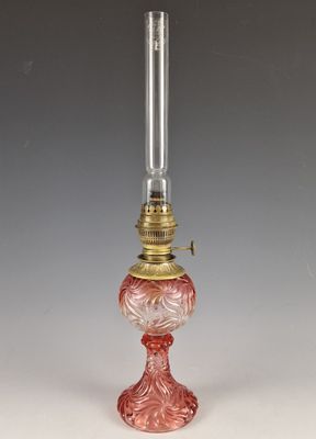 une lampe en verre rouge avec un pied doré, posée sur une surface blanche