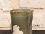 une tasse verte posée sur une table noire, avec un mur de briques en arrière-plan