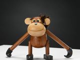 singe en bois tenant une paire de ciseaux sur une surface blanche