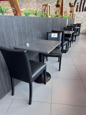 Dans un restaurant, des tables et des chaises sont alignées, et une enseigne est accrochée au mur.