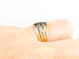 a woman ' s hand holding a gold ring with black and white stones
