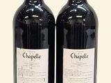 two bottles of red wine sitting next to each other on a white surface