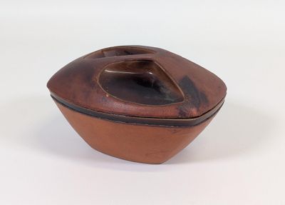 un petit bol marron avec un couvercle, posé sur une surface blanche