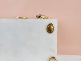 white marble clutch bag with gold rings on a pink background
