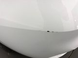 the front end of a white car with a dent on it