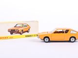une petite voiture orange posée à côté d'une boîte encore dans son emballage, sur une surface blanche