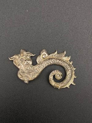 un gros plan d'une broche en forme de dragon doré posée sur une surface noire