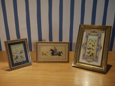 trois photos encadrées posées sur une table en bois, avec un mur rayé en arrière-plan