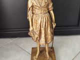 Une statue en or représentant une femme tenant une canne se dresse sur un sol carrelé