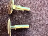 pair of gold tone cufflinks on a purple cloth