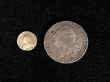 an old silver coin and a silver coin on a black surface