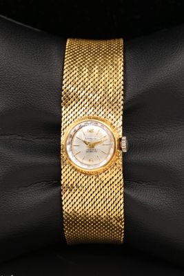un gros plan d'une montre-bracelet en or posée sur un coussin noir