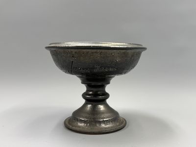 un bol ancien en argent, sur pied, posé sur un socle, sur fond blanc