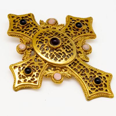 une photo d'une broche en forme de croix en or, ornée de pierres noires et roses