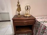 a small table with a clock on top of it next to a bed