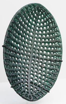 un panier vert perforé posé sur une surface blanche