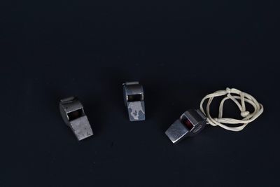 trois sifflets en métal et un cordon sur une surface noire