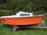 un petit bateau orange sur une remorque, dans l'herbe