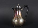 an antique silver coffee pot with a black handle on a black background