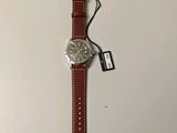 a close up of a watch on a white surface with a tag