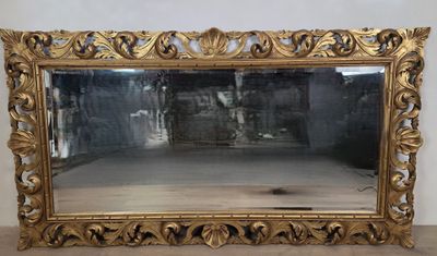 un miroir au cadre doré ouvragé posé sur un parquet