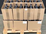 Des cartons de vin sont empilés sur une palette devant un mur noir