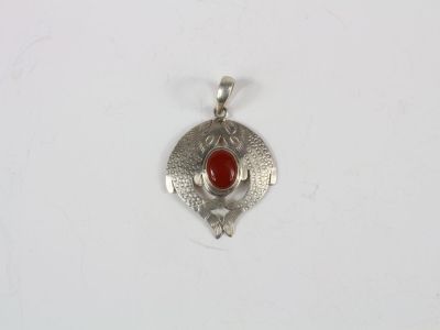 a close up of a silver pendant with a red stone