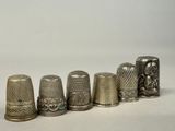 several silver thimbles lined up in a row on a white surface