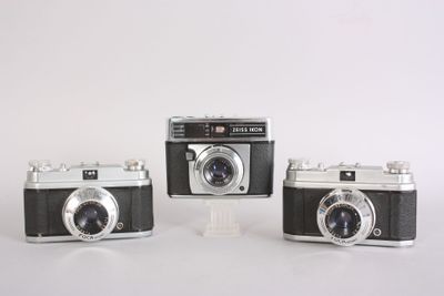 three old cameras sitting side by side on a white surface