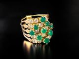 a close up of a gold ring with green stones on a black surface