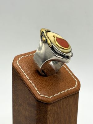 silver and gold ring with a red stone on top of a wooden block