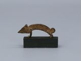 une petite sculpture en bronze représentant un chien, posée sur un bloc de bois