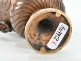 a bronze vase with a label on it on a white surface