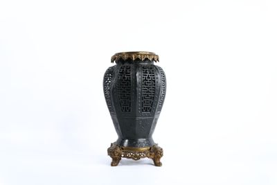 un vase noir posé sur un socle, sur une surface blanche