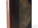 an old book with a brown cover sitting on top of a white table