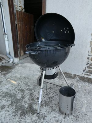 un barbecue noir posé sur le béton devant une maison