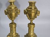 pair of antique brass urns on pedestals on grey background