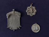 two silver pendants and a silver coin on a blue surface