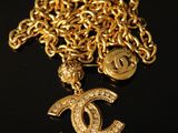 a close up of a gold chain with a chanel charm on it