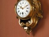 a gold clock hanging on the wall with a pendulum