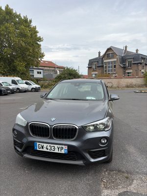 La BMW X1 est garée sur un parking devant une maison.