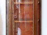 a glass display cabinet with a wooden shelf in the corner