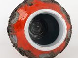 a red and black vase sitting on a white surface